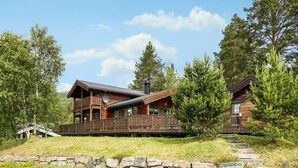 A wooden cabin with a balcony, surrounded by trees and a stone wall. - Stunning home in Bjorli with WiFi (Bjorli)