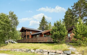 A wooden cabin with a balcony, surrounded by trees and a stone wall. - Stunning home in Bjorli with WiFi (Bjorli)