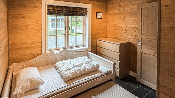 Ein Einzelbett mit Kopfteil, ein Fenster mit Blick auf Grünflächen und ein Holzschrank.