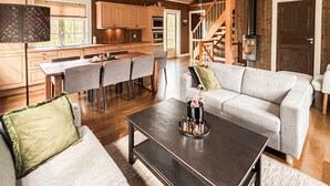 Eine moderne Küche mit Holzausstattung, eine Essecke mit Tisch und Stühlen, ein graues Sofa und eine Treppe, die zu einem Schlafzimmerboden führt.
