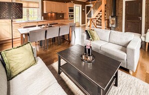 Eine moderne Küche mit Holzausstattung, eine Essecke mit Tisch und Stühlen, ein graues Sofa und eine Treppe, die zu einem Schlafzimmerboden führt.