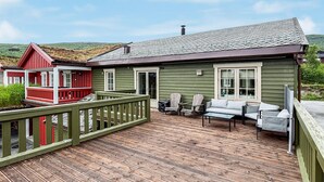 Eine Holzterrasse mit Gartenmöbeln, ein rot- und grün gestrichenes Gebäude und eine Aussicht auf die Landschaft.