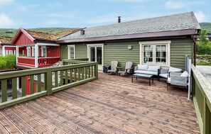 Eine Holzterrasse mit Gartenmöbeln, ein rot- und grün gestrichenes Gebäude und eine Aussicht auf die Landschaft.