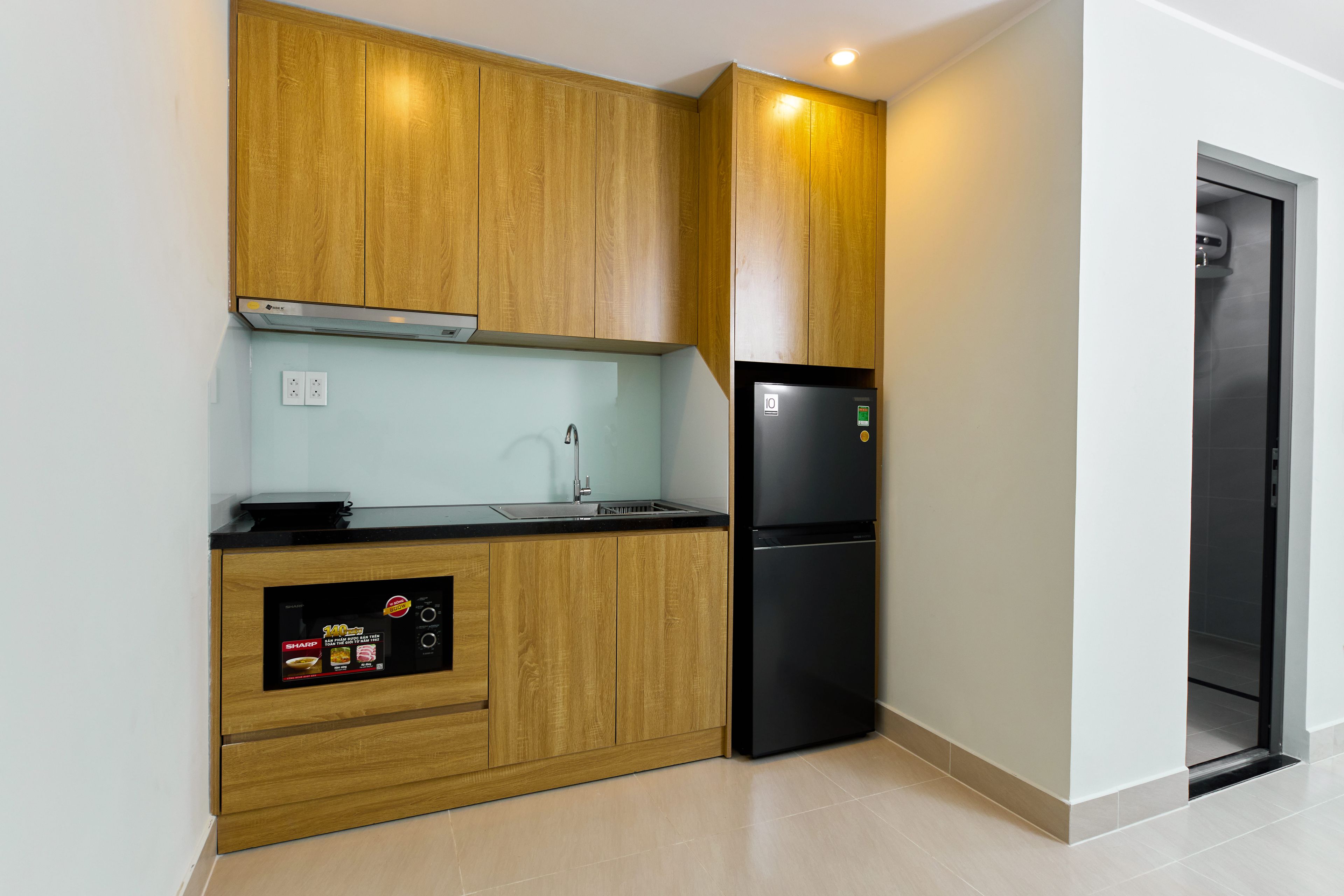 A compact kitchen with wooden cabinets, a black refrigerator, and a built-in microwave.