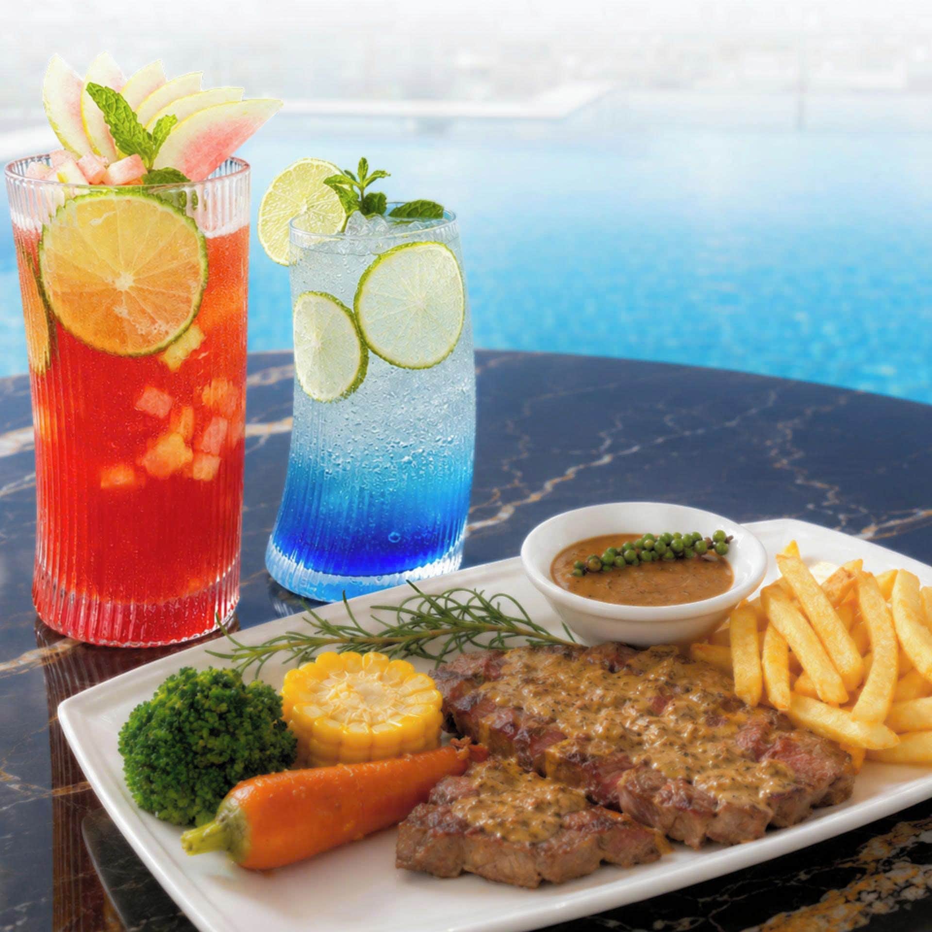 A meal with steak, fries, and vegetables, and two drinks with lime and mint garnish.