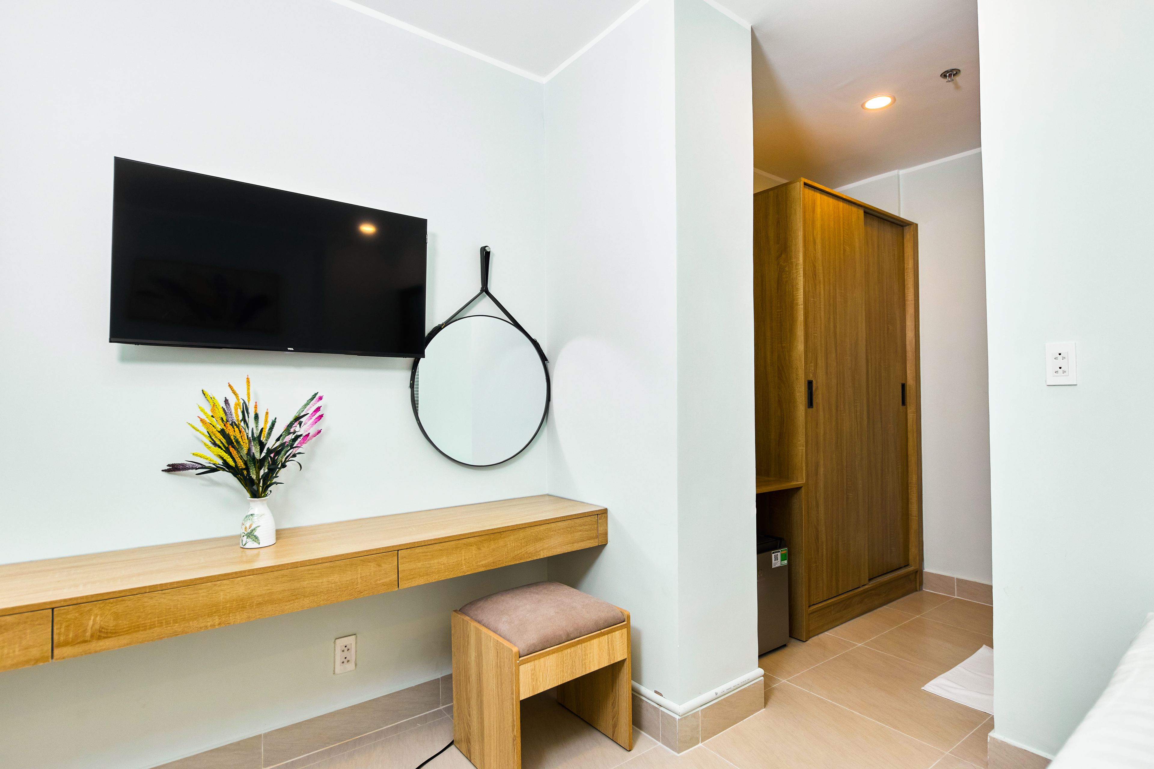 Un baño moderno con tocador de madera, un espejo, un televisor montado en la pared y una puerta de madera.