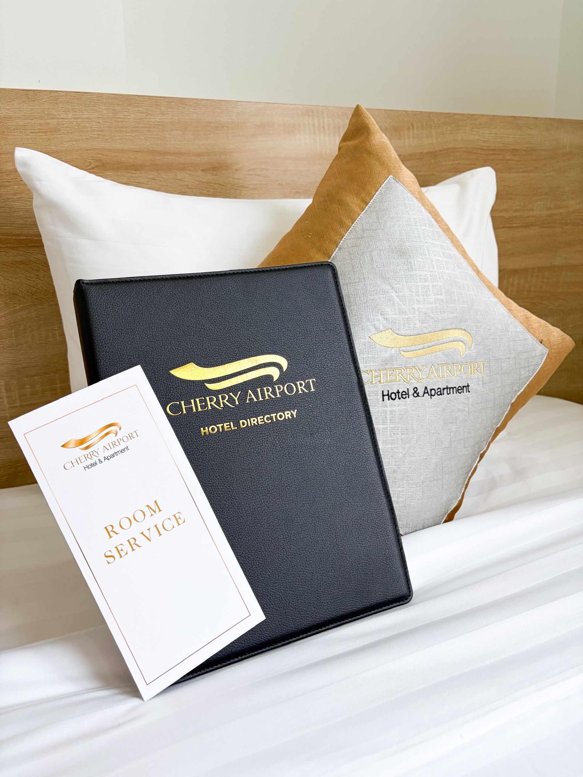 Une chambre d’hôtel avec un lit, des oreillers, un annuaire à la couverture en cuir noir et une carte de service en chambre blanche.