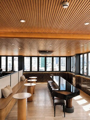 Un intérieur moderne avec une longue table à manger, de nombreux espaces pour s’asseoir et de grandes fenêtres offrant une vue sur la ville.