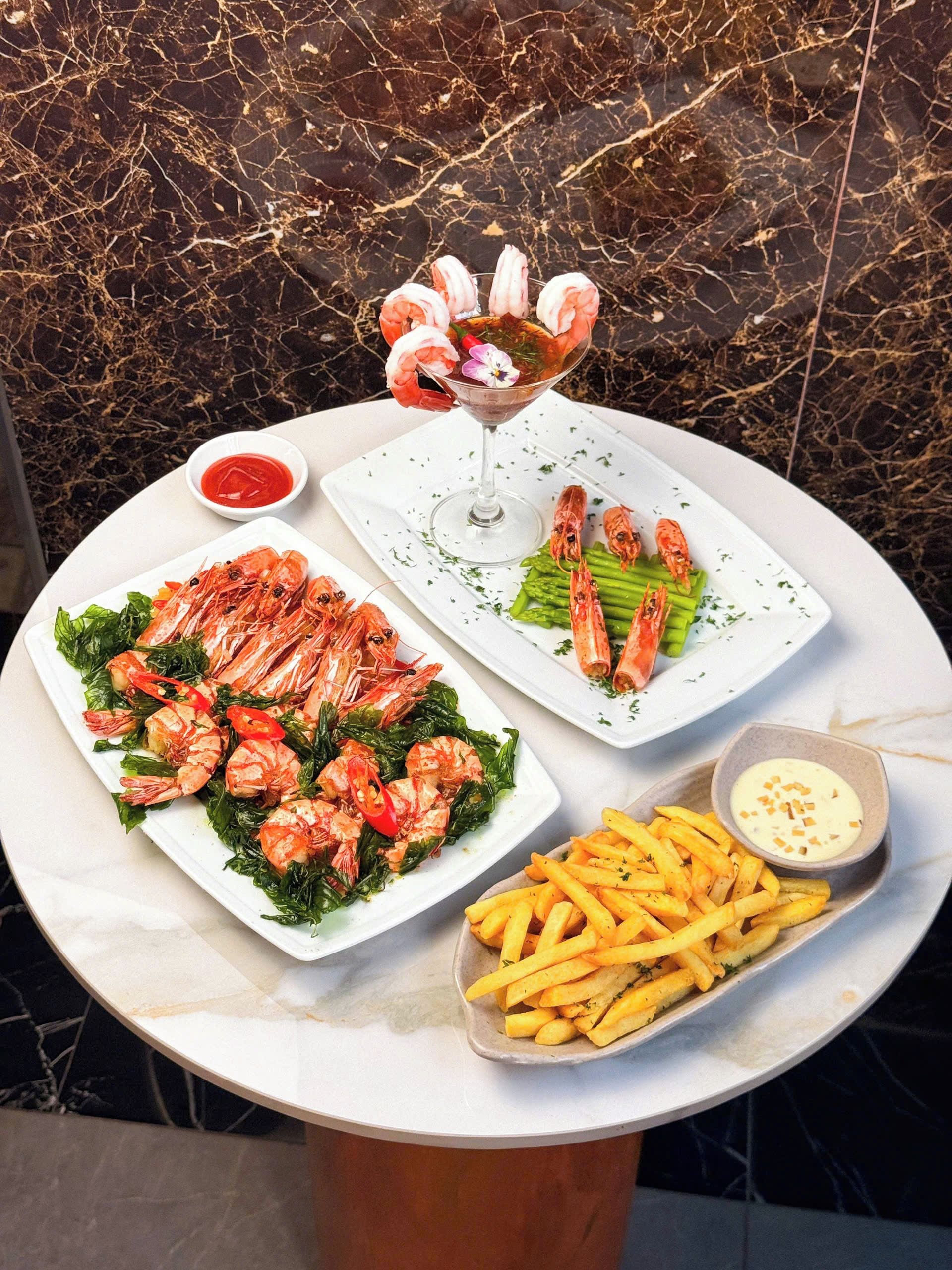 A table with seafood dishes, a glass of drink, and a side of fries.