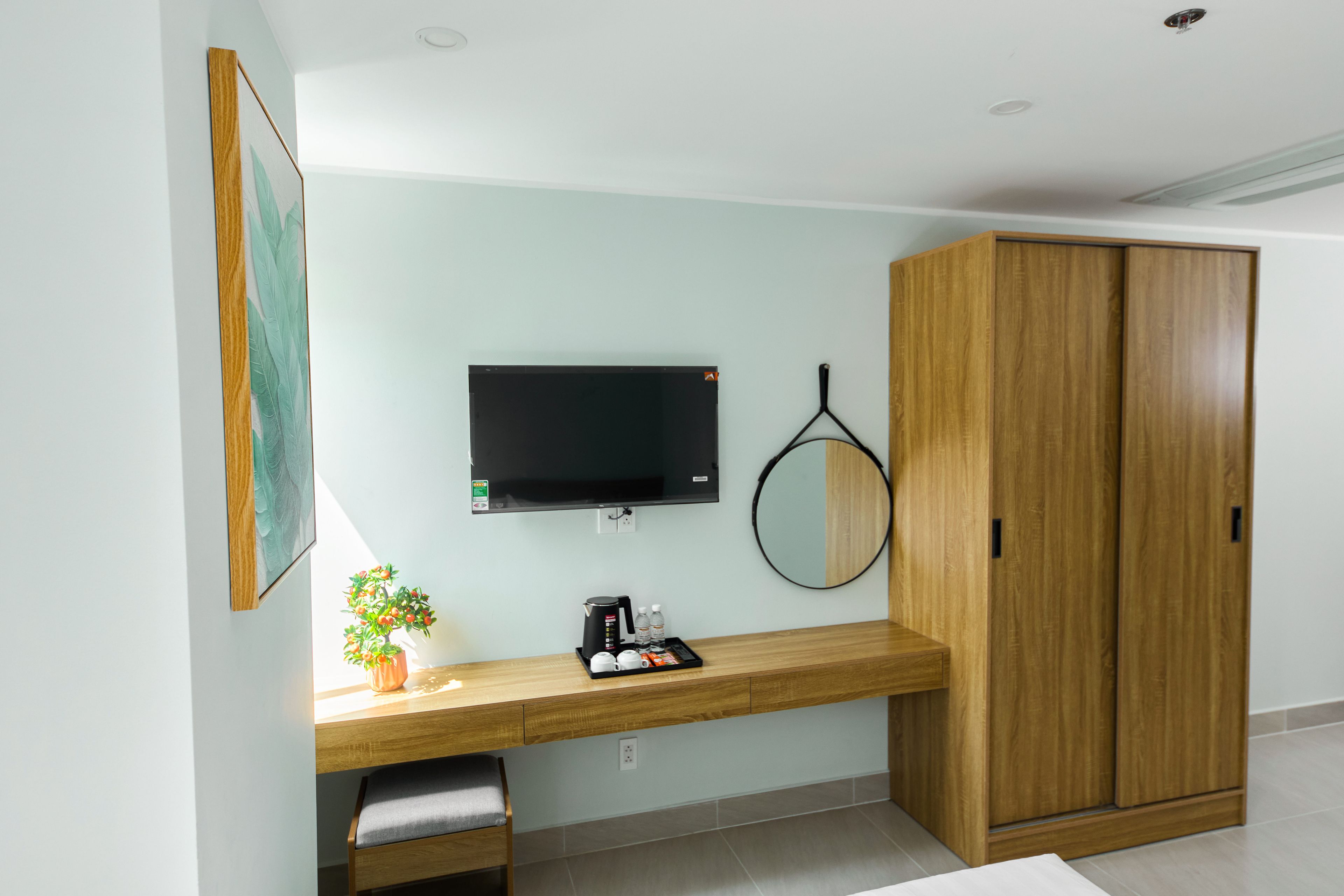 A modern room with a wooden desk, a television mounted on the wall, a wardrobe, and a potted plant.