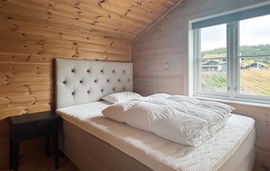 Ein Schlafzimmer mit Holzboden, einem gesteppten Kopfteil, einem Bett mit weißer Bettwäsche und einem Fenster mit Blick auf ein Haus und einen Rasen.
