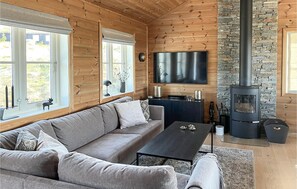 Ein gemütliches Blockhaus-Interieur mit einer Couch, einem Couchtisch, einem Fernseher, einem Kamin aus Stein und einem Fenster mit Blick.