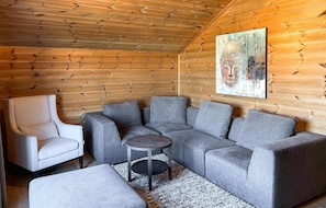 Ein gemütliches Zimmer mit einem grauen Ecksofa, einem weißen Sessel und einem kleinen runden Tisch.