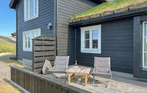 Ein dunkles Holzhaus mit verdeckter Veranda, zwei Stühlen, einem Tisch und einer Flasche.