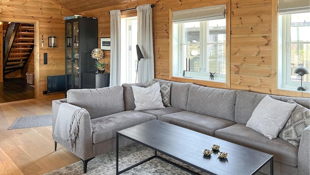 Una sala de estar moderna con un sofá seccional gris, una mesa de centro y una escalera que conduce a otro nivel.