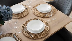 Un tavolo da pranzo imbandito con piatti bianchi, posateria e bicchieri di vetro trasparenti su tovagliette intrecciate.
