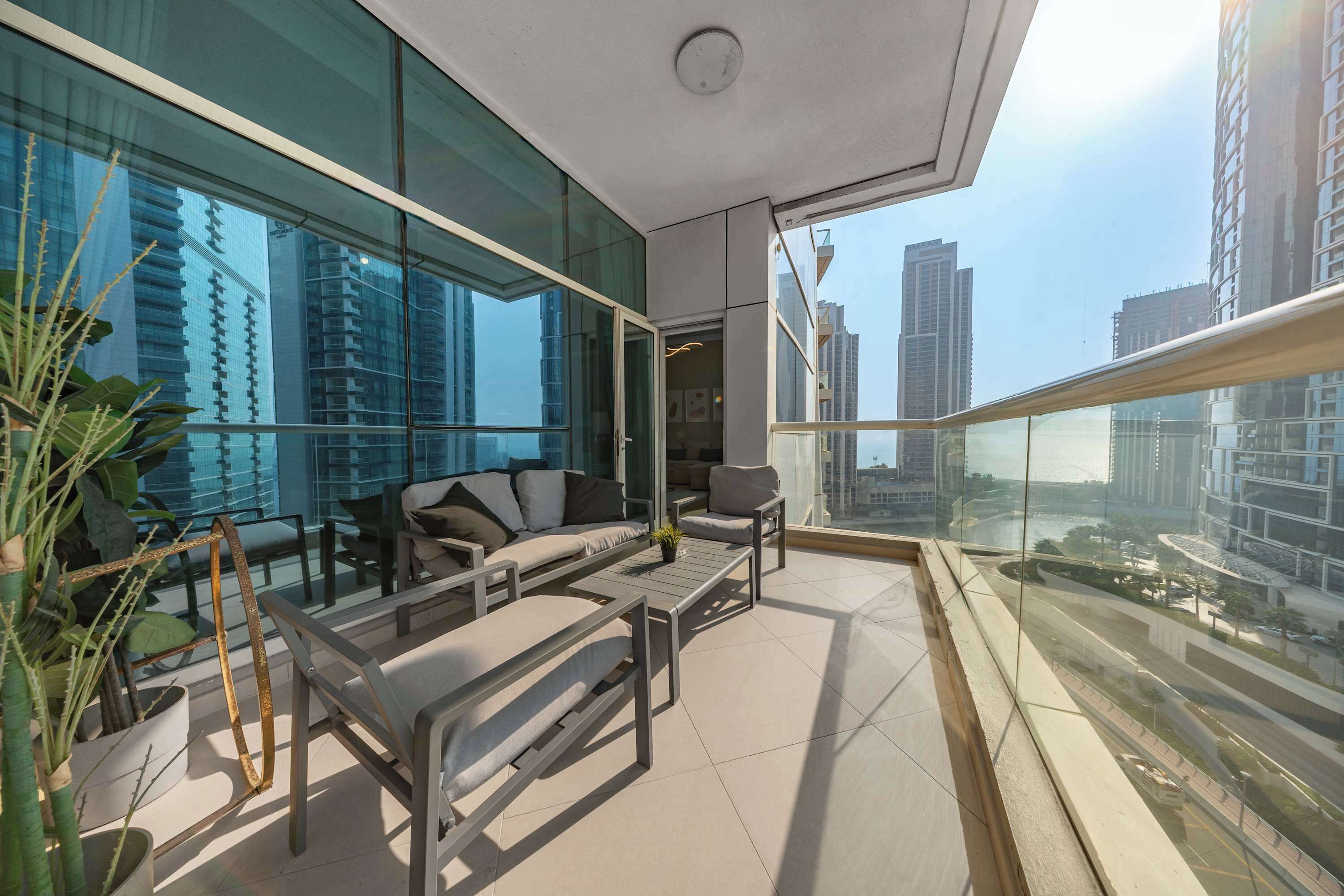 A modern balcony with a sofa, chairs, and a coffee table, overlooking a cityscape.