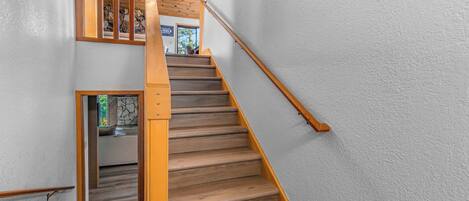 A wooden staircase with a handrail, white walls, and a stone accent wall.
