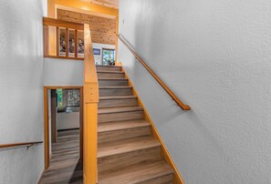 A wooden staircase with a handrail, white walls, and a stone accent wall.