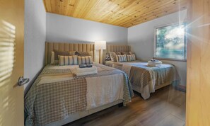 A bedroom with two beds, a wooden ceiling, and a window with blinds.