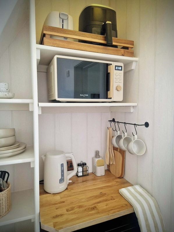A kitchen with a microwave, kettle, and hanging utensils.
