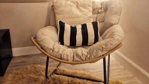 Una silla de ratán con un tapete mullido, una pared de color claro y luces colgantes.
