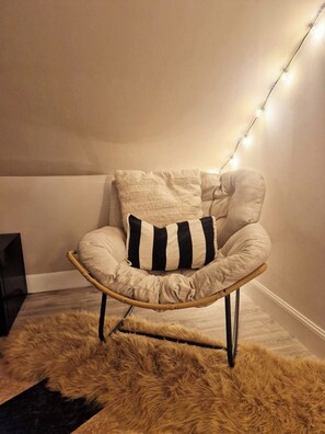 Una silla de ratán con un tapete mullido, una pared de color claro y luces colgantes.
