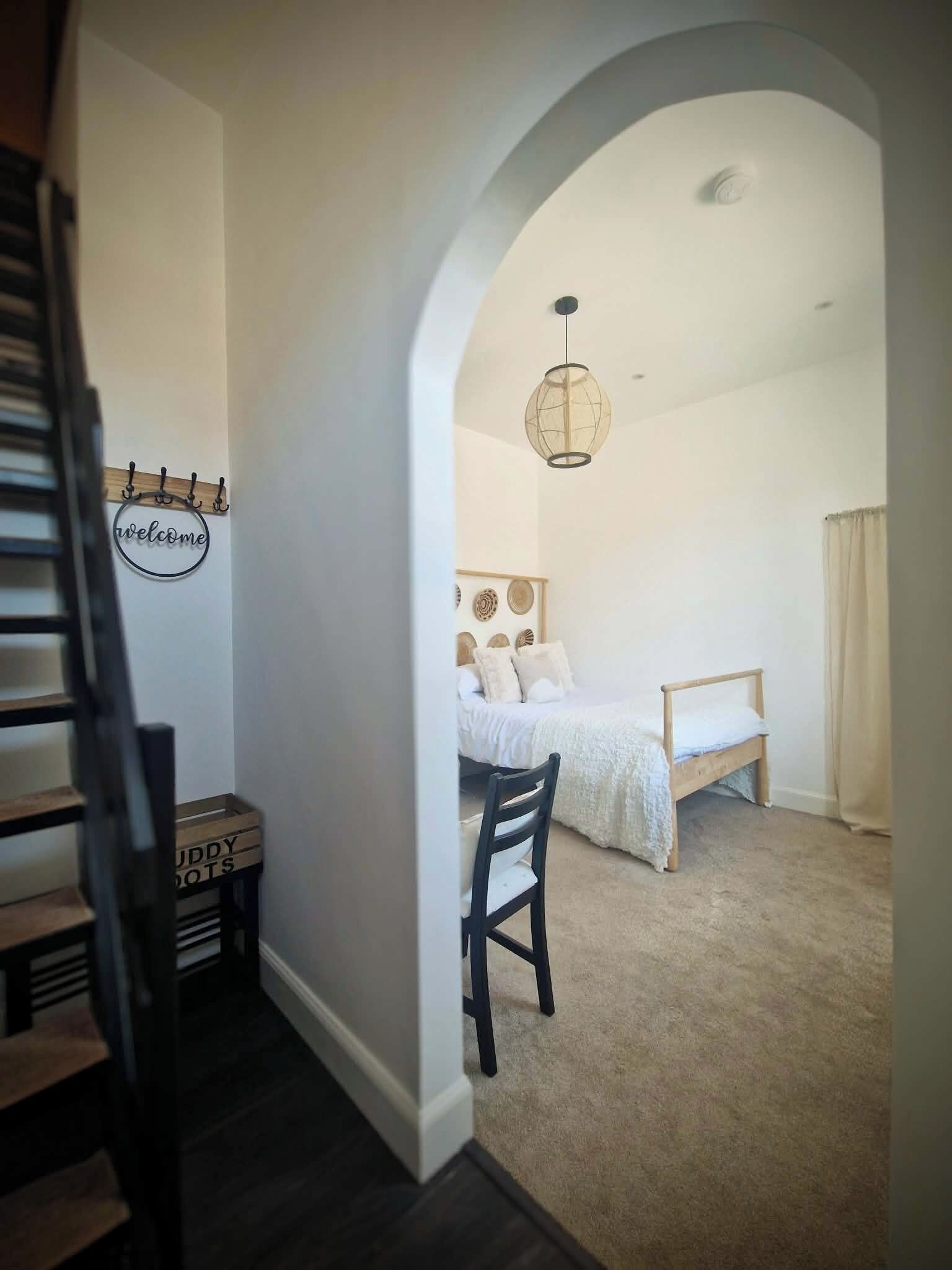 Une chambre à coucher avec un lit, une chaise, un luminaire suspendu et un panneau indiquant « Bienvenue » sur le mur.