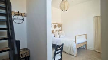 Une chambre à coucher avec un lit, une chaise, un luminaire suspendu et un panneau indiquant « Bienvenue » sur le mur.