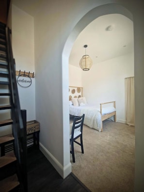 A bedroom with a bed, a chair, a hanging light fixture, and a 'welcome' sign on the wall.