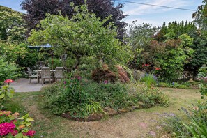 Un jardín con una mesa y sillas de madera, rodeado de plantas y flores diversas.