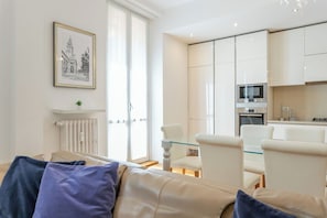 A modern living room with a sofa, a dining table, and chairs. There is a kitchen area with white cabinets and appliances. A framed picture hangs on the wall. - Apartment in Milan with 2 bedrooms sleeps 4 (Milan)