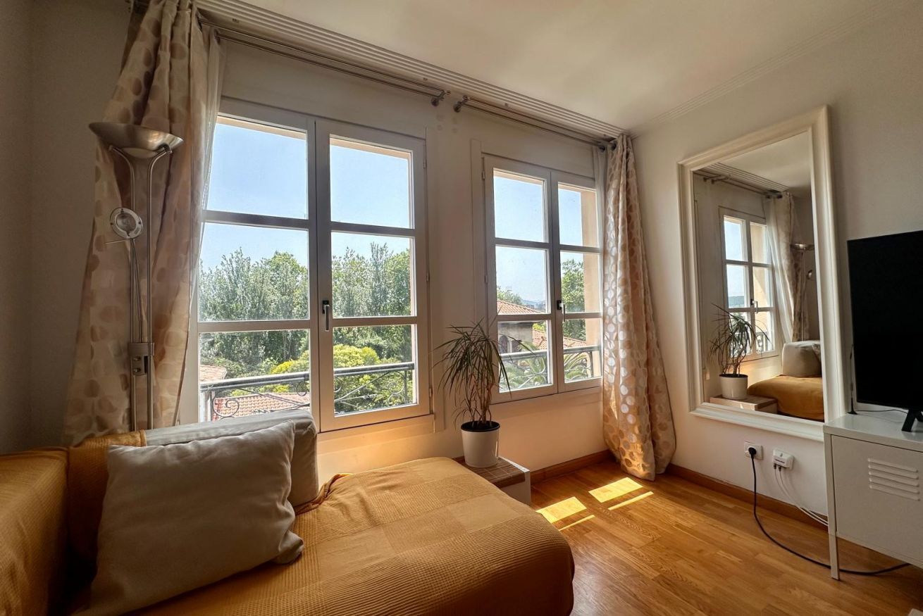 A room with a bed, a desk, a TV, and large windows.