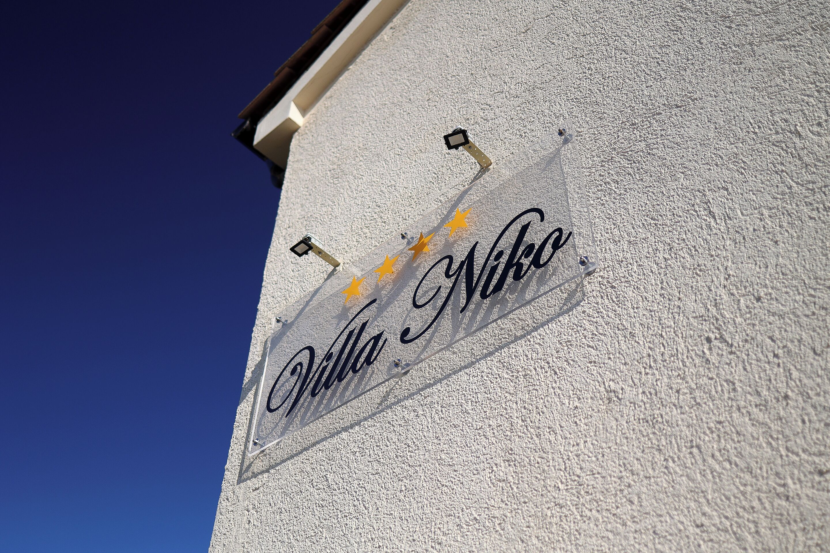 Ein Schild mit dem Schriftzug 'Villa Niko' an einer strukturierten Wand.