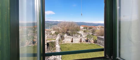 A view through a window with a stone building, grassy area, and distant mountains.
