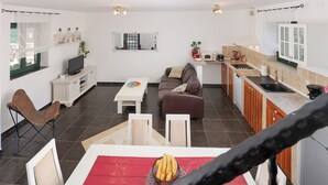 Ein modernes Wohnzimmer mit einer Couch, einem Esstisch mit roter Tischdecke und einer Küchenzeile mit Spüle und Schränken.