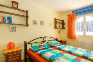 A bedroom with a bed, a nightstand, a shelf with books, a window with curtains, and a radiator. - Casa Nuestro Sue o Para 4 Personas (Calpe)