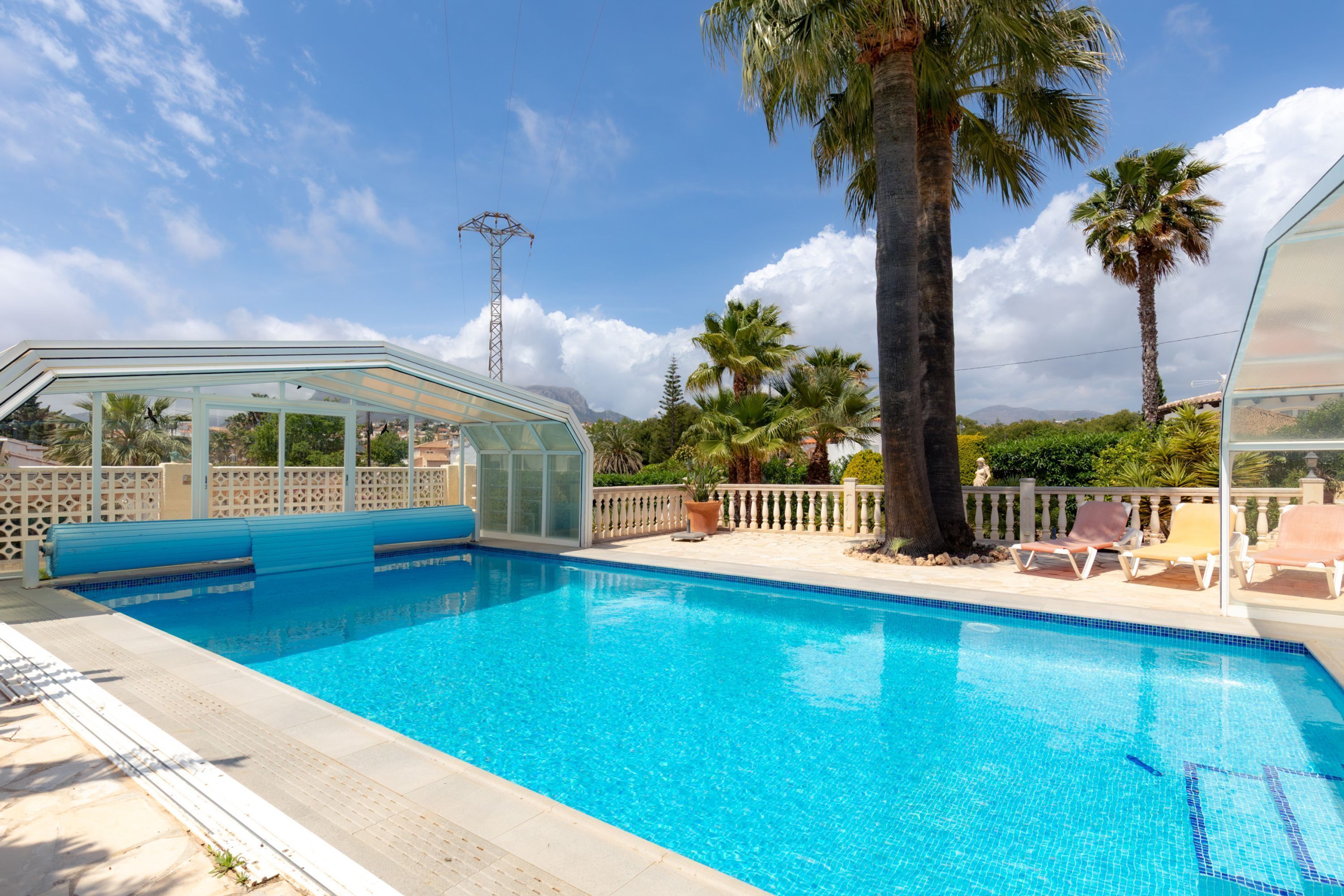 Une piscine à l’eau d’un bleu cristallin, entourée de palmiers et dotée d’un salon fermé par des baies vitrées.