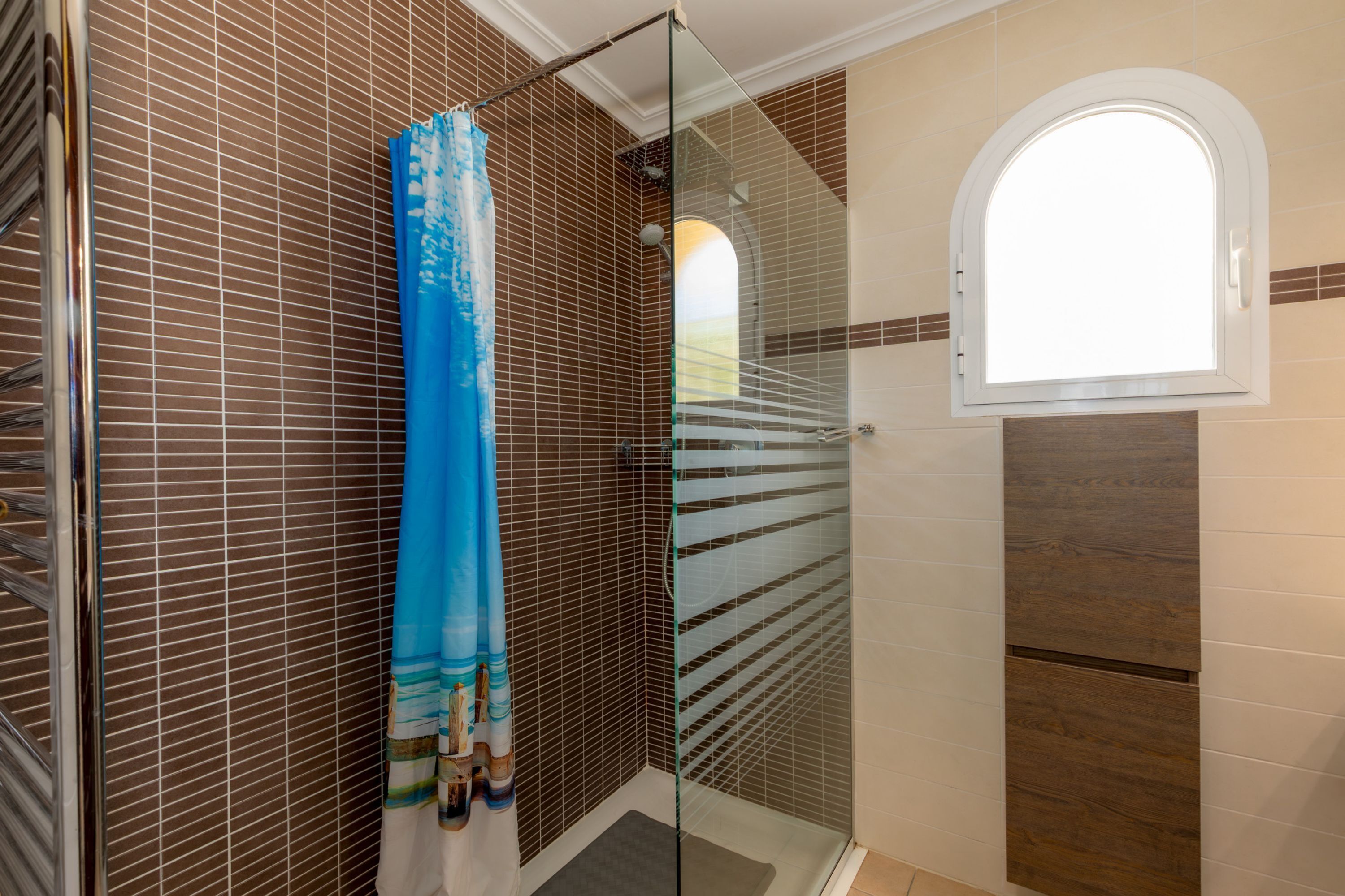 Baño con cabina de ducha de vidrio, cortina de ducha azul y una ventana.