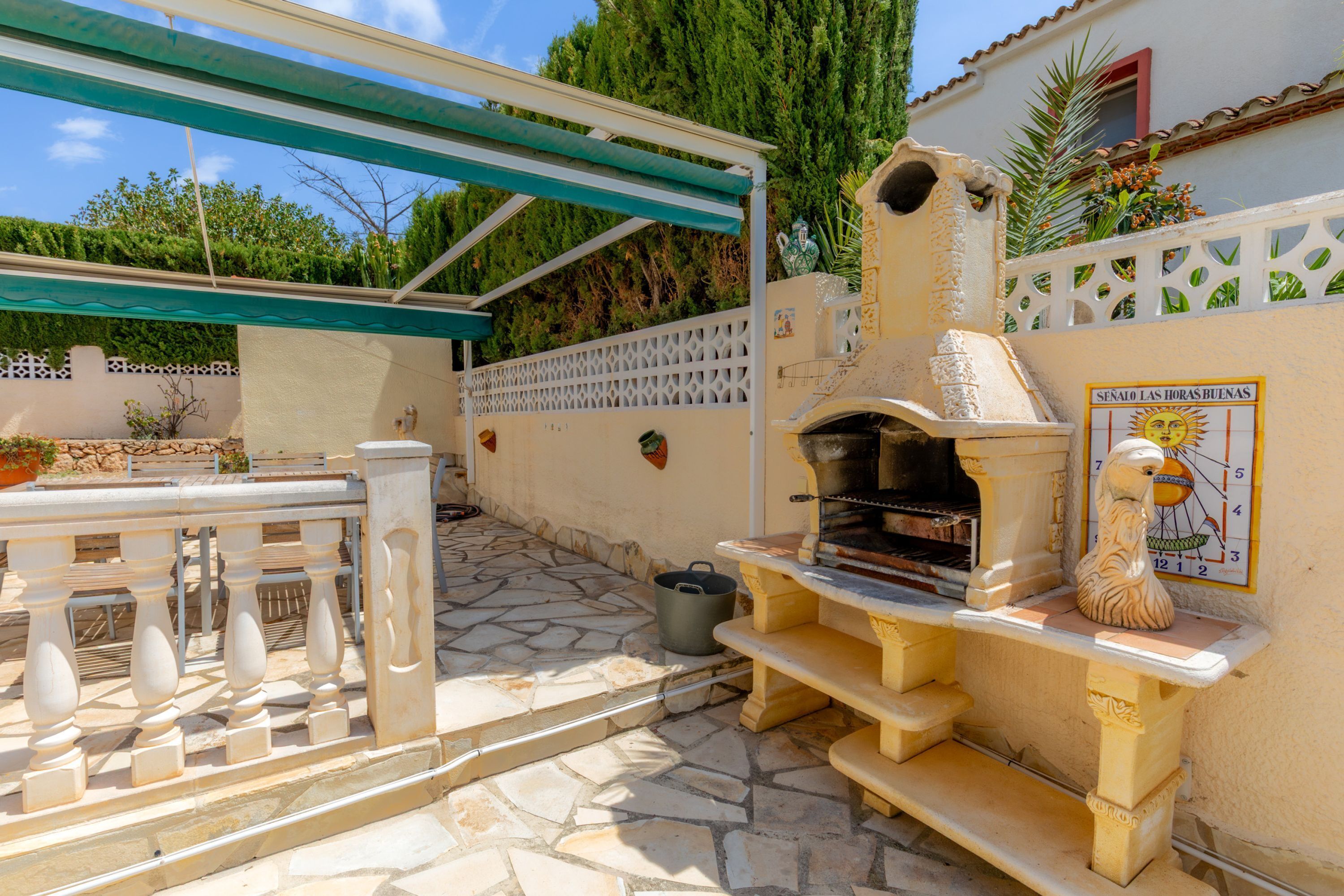An outdoor patio with a stone floor, a grill, a white fence, and a pergola.