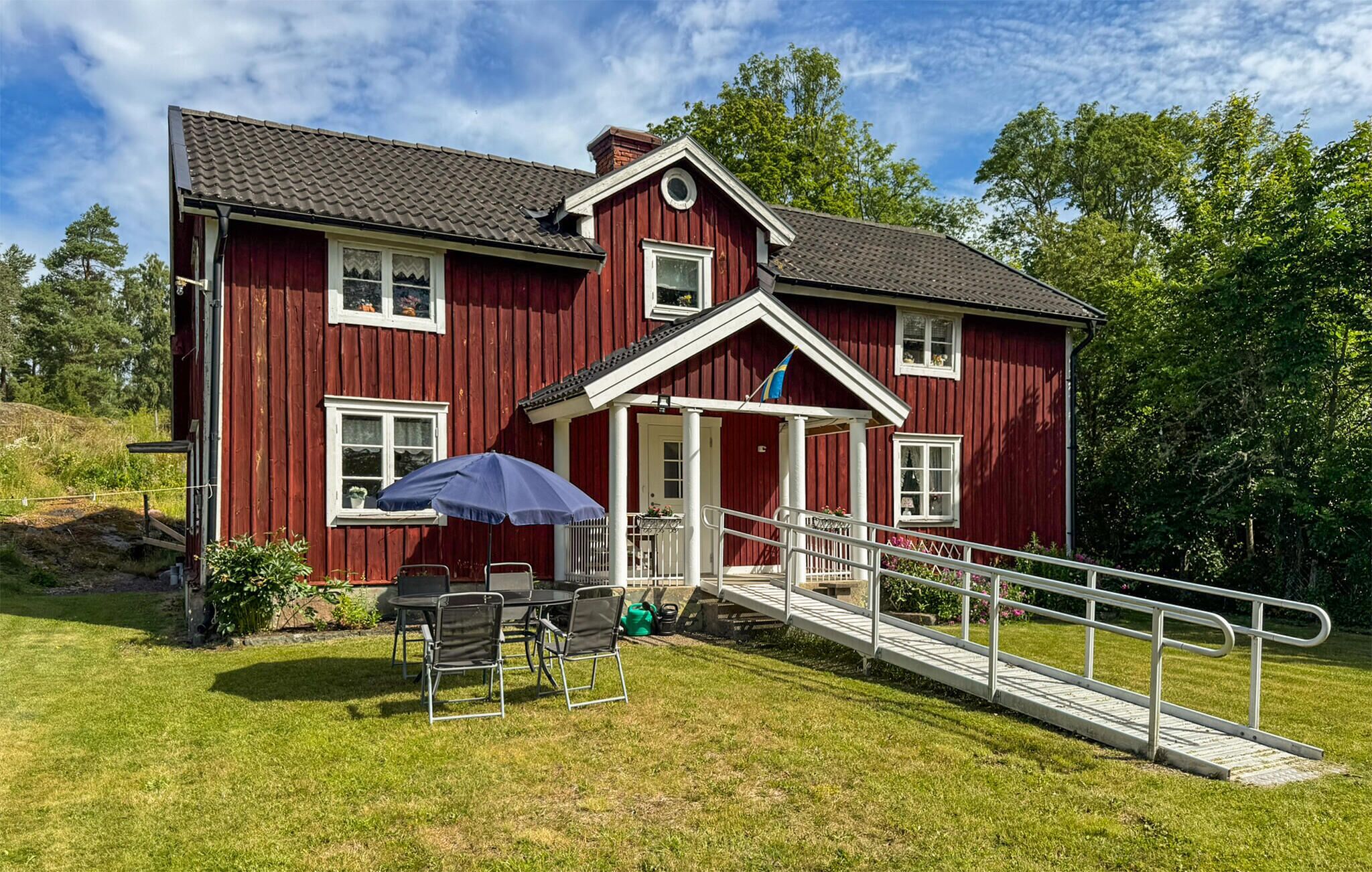 A red wooden house with a porch, a small table with chairs, and a wheelchair ramp.