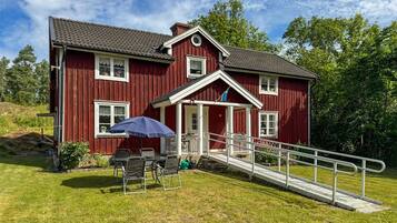 A red wooden house with a porch, a small table with chairs, and a wheelchair ramp.