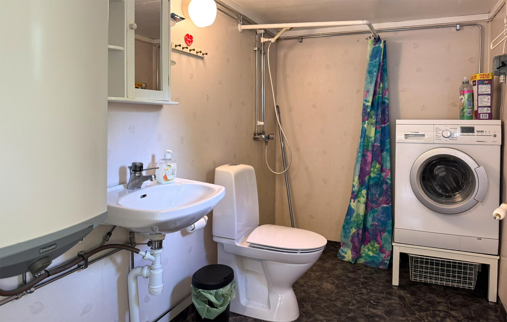 Ett litet badrum med handfat, toalett, dusch och tvättmaskin.