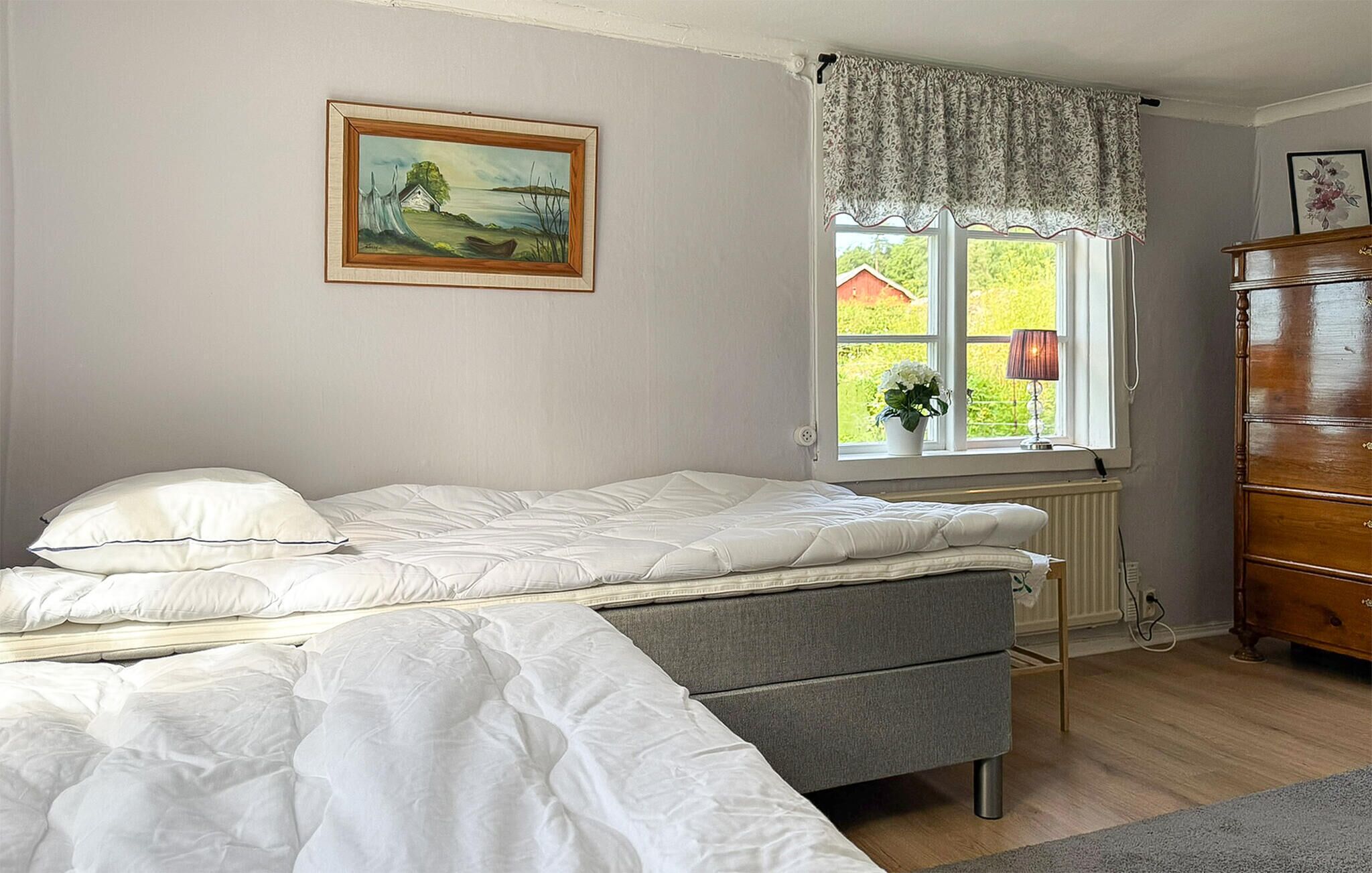 A bedroom with a bed, a dresser, a window with a view, and a painting on the wall.