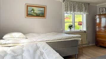 A bedroom with a bed, a dresser, a window with a view, and a painting on the wall.