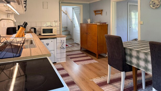 A compact kitchen with a microwave, stove, and wooden counter. There is a dining area with a checkered tablecloth and chairs. - Cozy home in Tranås with WiFi (Tranås)