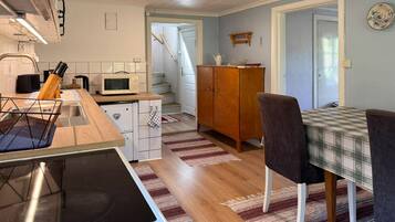 A compact kitchen with a microwave, stove, and wooden counter. There is a dining area with a checkered tablecloth and chairs.