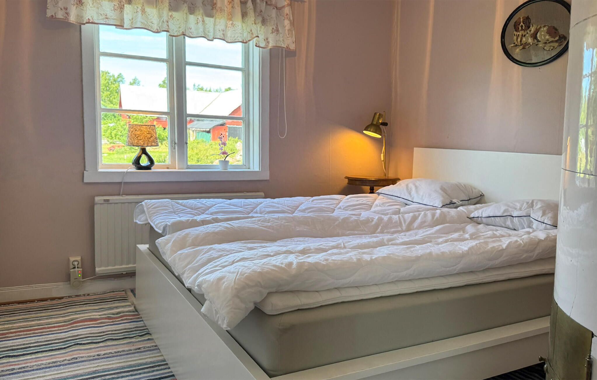 A bedroom with two beds, a window with a view, a lamp, and a radiator.