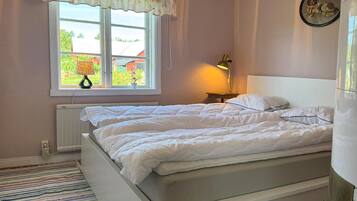 A bedroom with two beds, a window with a view, a lamp, and a radiator.