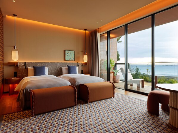 A modern hotel room with two beds, a large window, and a balcony with a view.